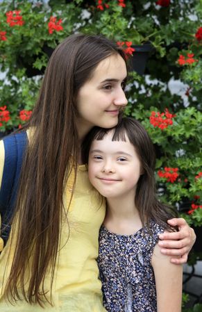 Two sisters hugging each other outdoors near a garden