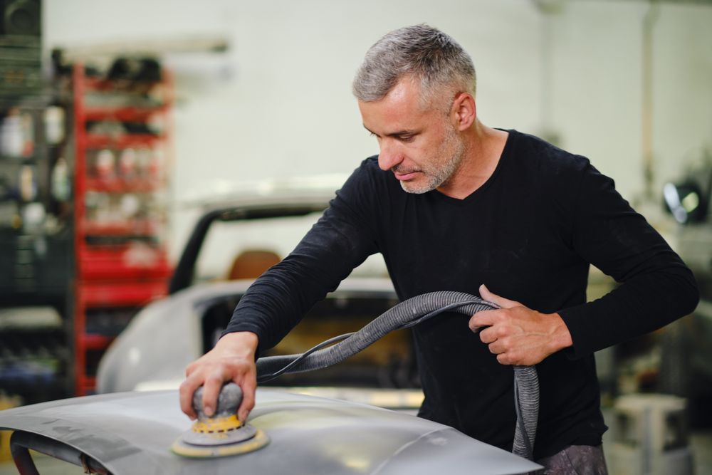 Mechanic grinding paint from car detail