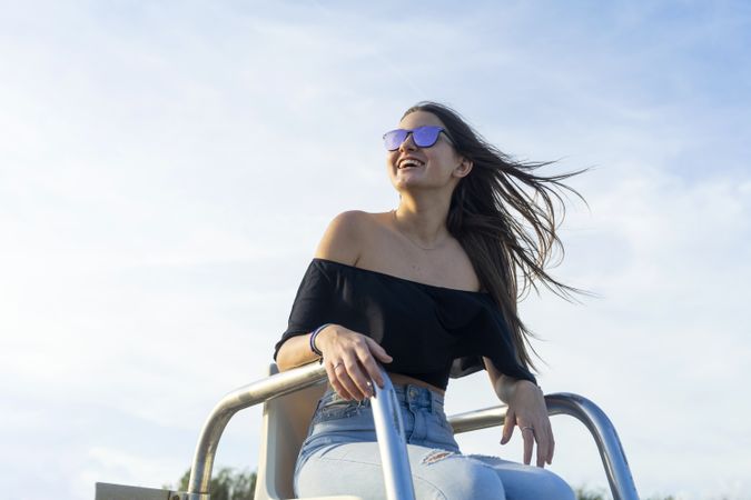 Young woman and sunglasses sitting outdoors while smiling and looking away with the wind in her hair