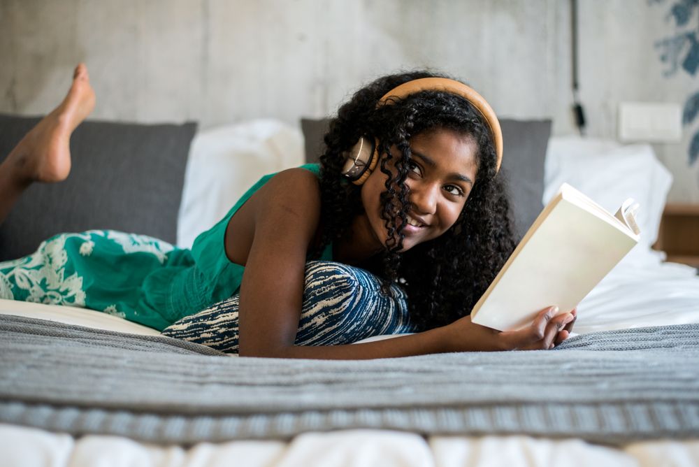 Black teenage reading a book on bed