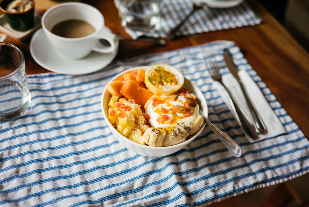 Table set with bowl of fresh fruit breakfast with nuts, honey and yogurt
