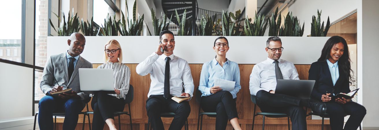 Group of people sitting and working in a row in a bright office, wide shot