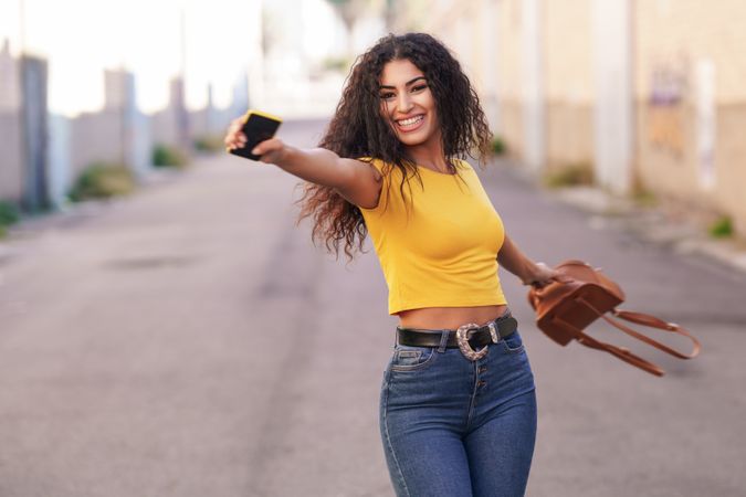 Happy woman spinning around in center of street holding bag and phone