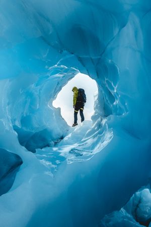 Person with backpack standing beside ice cave