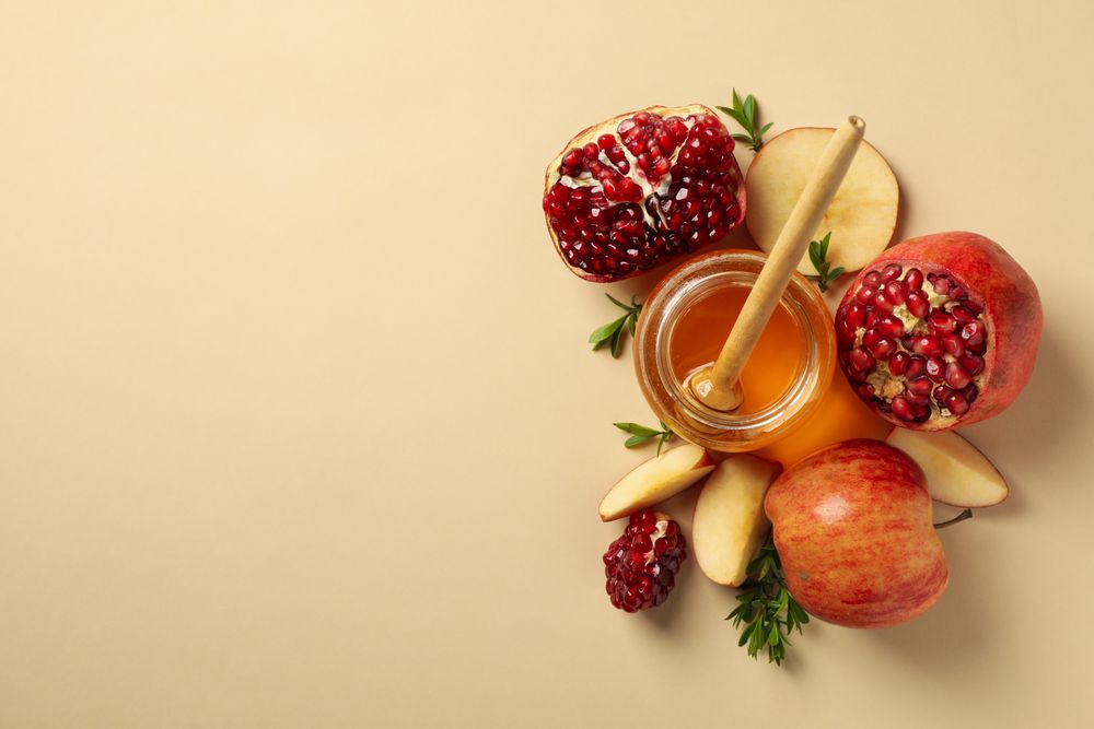 Looking down at open pomegranate, honey pot and sliced apple