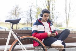 Man relaxing with bicycle checking smartphone while sitting on bench bxAvGj