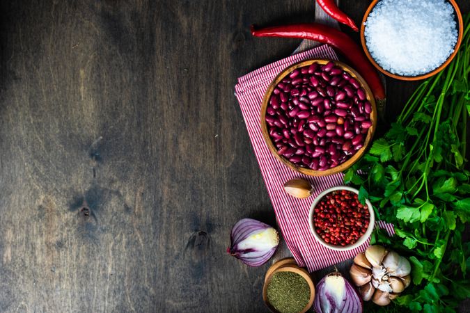 Bowl of red kidney beans and red peppercorns on kitchen towel with garlic, cilantro, peppers and onions