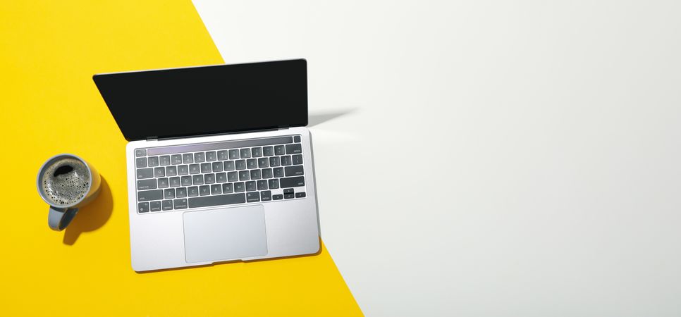 Banner of laptop with blank screen with mug of coffee on dual tone yellow background with copy space