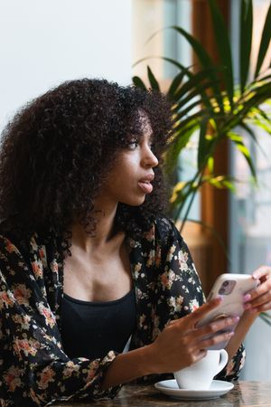 Black woman using smartphone at table with hot drink