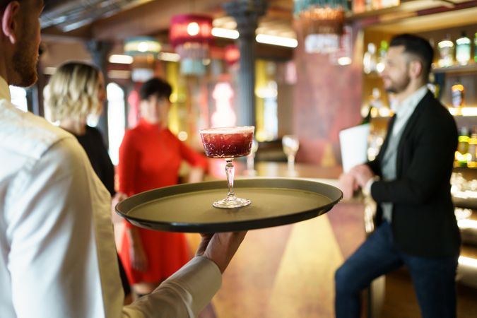 Bartender walking with red cocktail on serving tray
