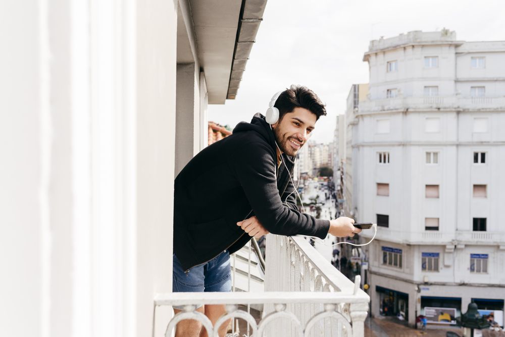 Young happy man holding smartphone on balcony