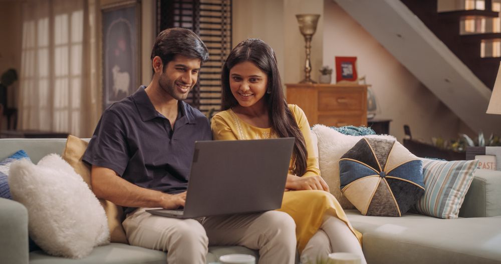 Adorable Young Indian Couple Using Laptop, Sitting on Home Sofa.