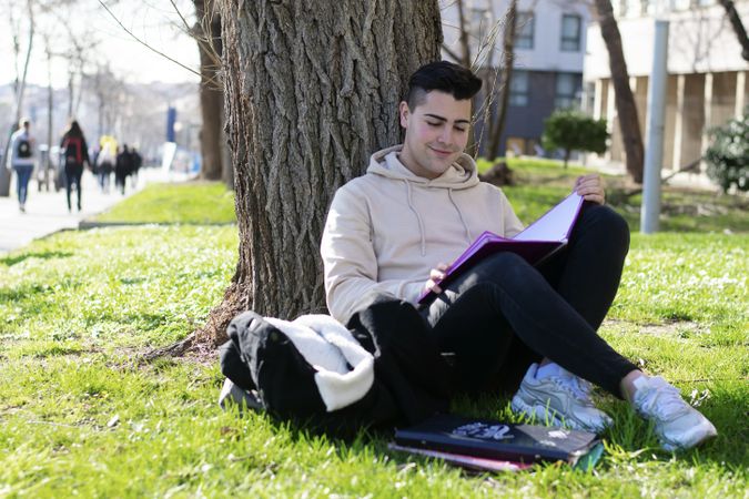 Young man leaning back on a tree and reading a book