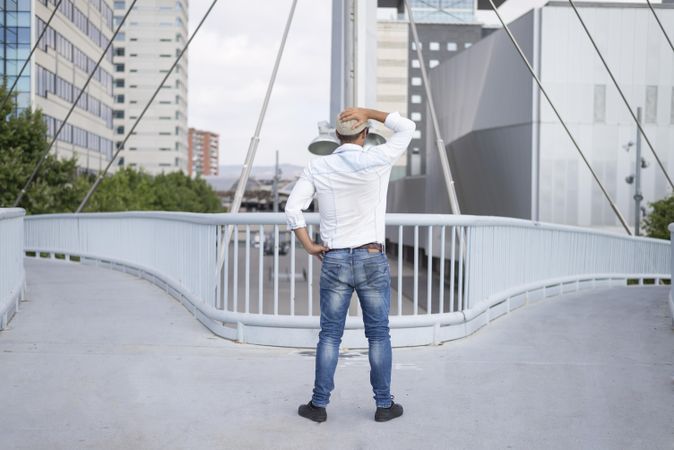 Male in denim standing with hands on head in confusion on bridge above city
