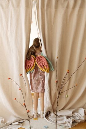 Anonymous girl with colored costume wings by curtain