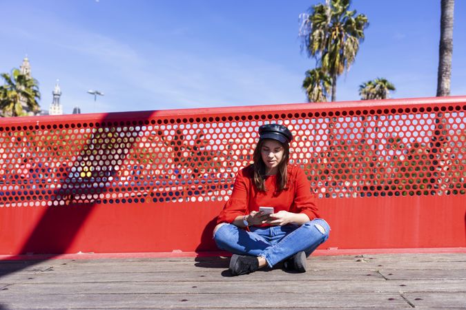 Woman in red sitting cross legged using a mobile phone outdoors