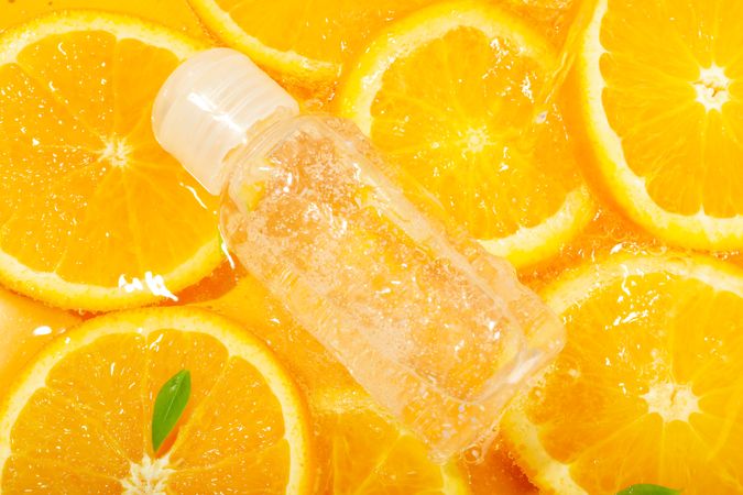 Top view of orange slices with leaves soaking in fresh water with plastic bottle