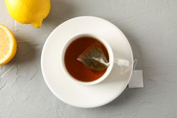 Cup of tea with tea bag and lemons on grey background, top view