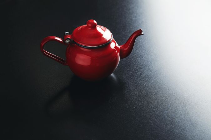 Shiny red tea pot on dark table