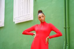 Serious female in red zipped up shirt standing outside green building