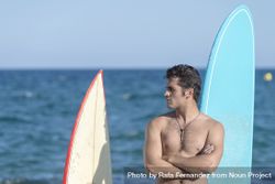 Male surfer standing with boards in front of the ocean 5RQQr0