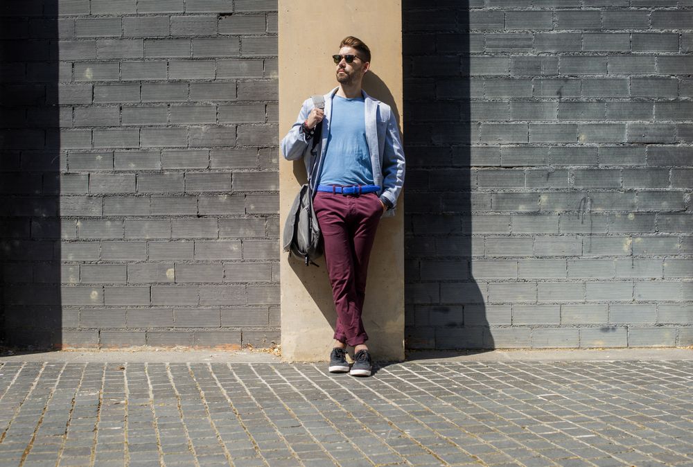 Man wearing casual clothes while leaning on a building wall outside with bag