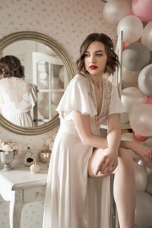serious young woman standing near round mirror in boudoir