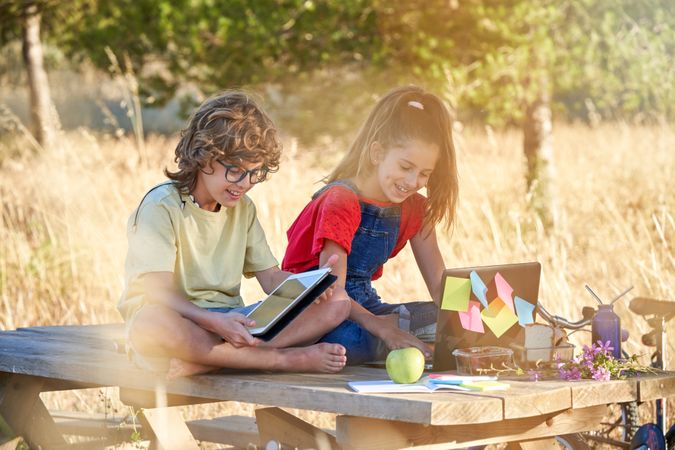 Children laughing while browsing tablet and laptop in nature