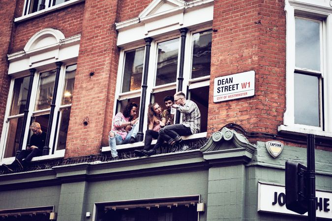 London, England, United Kingdom - July 7th, 2019: Group of people sitting out on a window ledge
