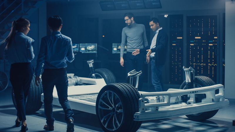 Team of Automotive Engineers Discussing and Designing Electric Car Platform Chassis Prototype, Taking Measures