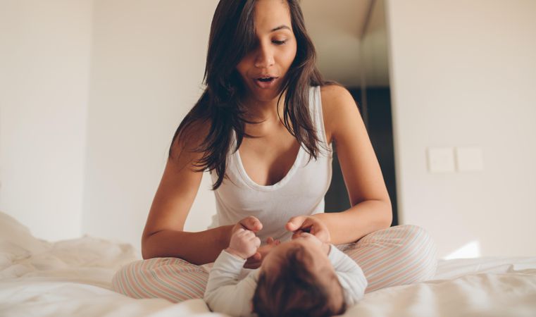 Woman sitting on bed and playing with her baby at home