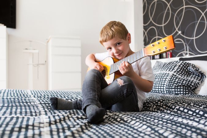 Young blonde boy playing toy guitar