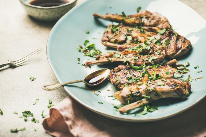 Plate of grilled lamb chops with parsley garnish on light blue plate, horizontal composition