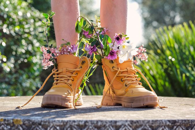 Crop person wearing boots with flowers standing in garden