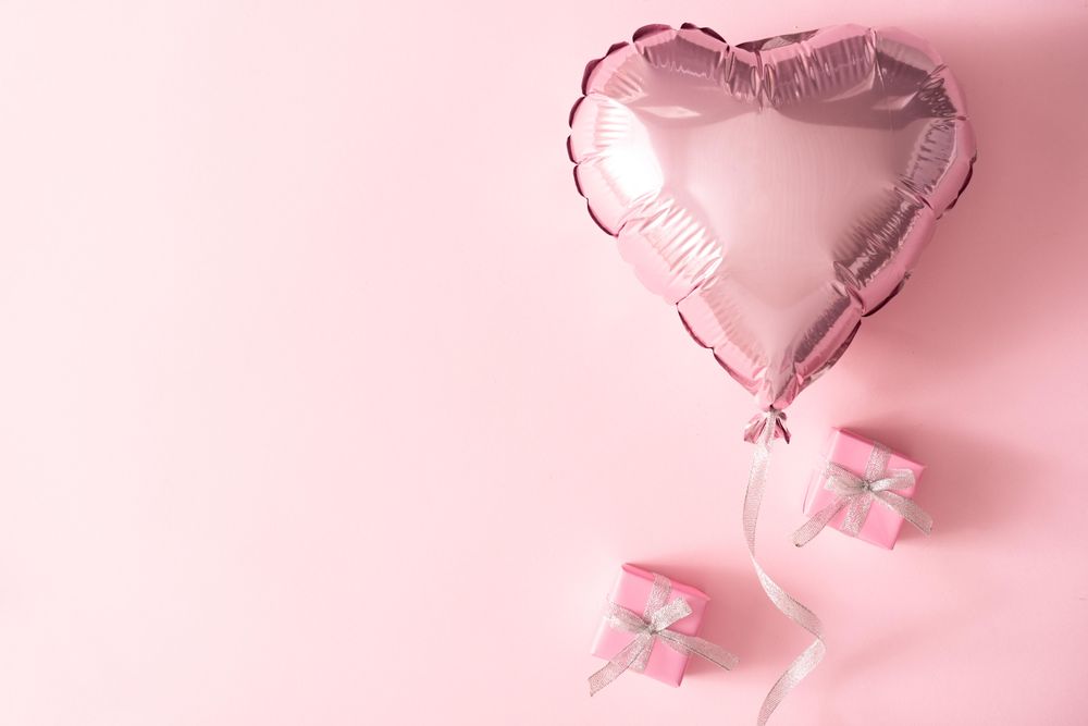 Pink foil balloon and wrapped presents against pink background