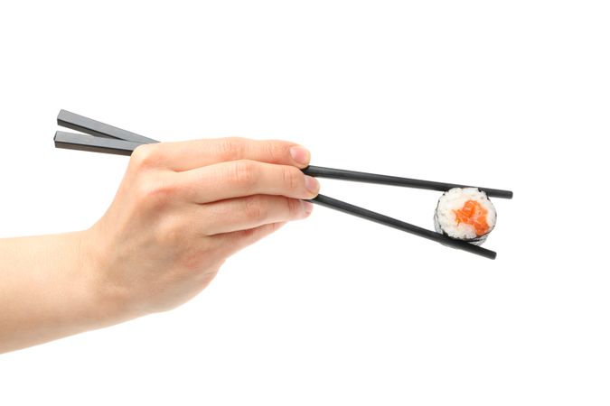 Female hand with chopsticks holds sushi roll, isolated on plain background