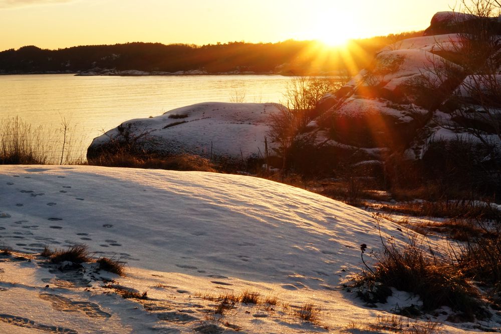 Rocky peaceful shore with snow crust in sunrays