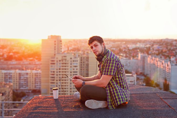 Male sitting on roof with tablet and cup of coffee