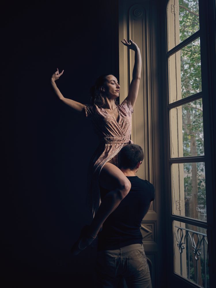 Ballerina on shoulder of faceless dancer near window