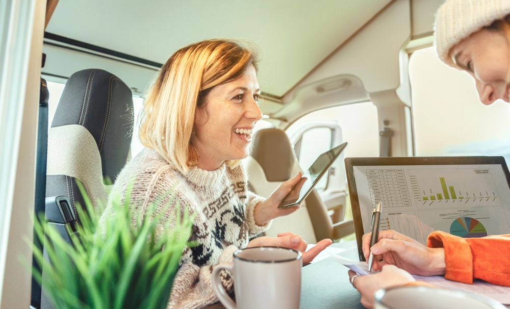 Female friends smiling while working remotely in back of van while camping