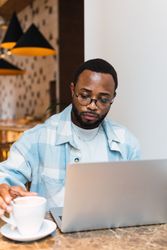 Black man with coffee browsing laptop