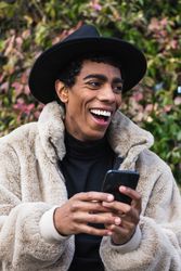 Stylish happy hispanic man with smartphone on street