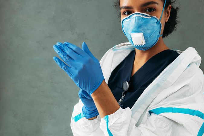 Black woman in facemask putting on protective gloves