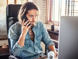 Attentive male browsing PC and talking on mobile in flat