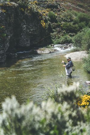 Confident man fishing with rod while standing in river stream