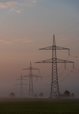 Electricity pylons in a row through fog at sunrise, in a german village