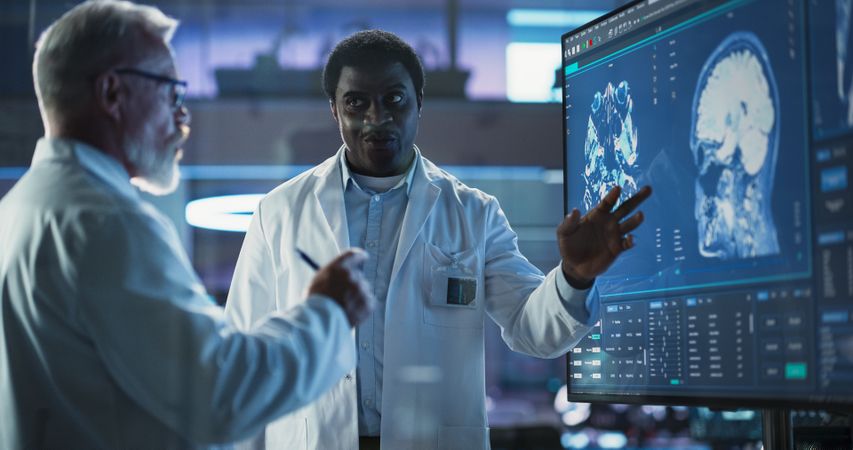 Neuroscience Laboratory Meeting: Black Male Scientist And White Surgeon Discussing MRI Brain Scan On TV Display.
