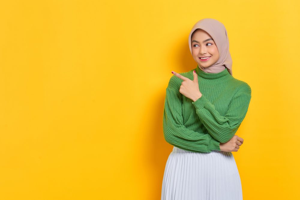 Excited woman in headscarf pointing her finger up towards the side at copy space