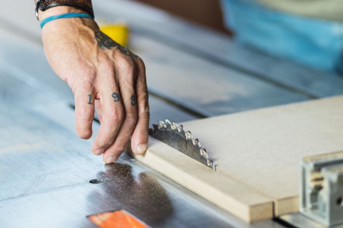 Crop male carpenter cutting wood with circular saw