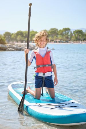 Boy with paddle standing on SUP board among sea